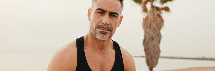 Close up, middle-aged muscular man looks at the camera while sitting on the promenade after...