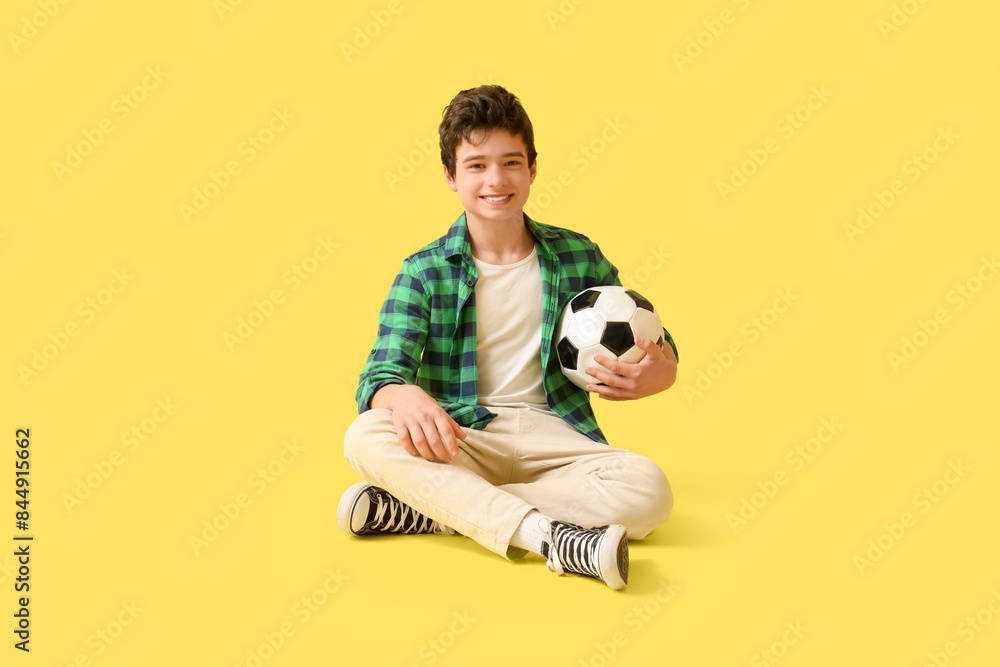 Poster Teenage boy with soccer ball sitting on yellow background