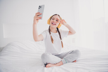 Portrait of cute adorable lovely girl sitting bed recording video weekend v-sign white light interior indoors