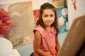 Young girl in art class painting on canvas at workshop