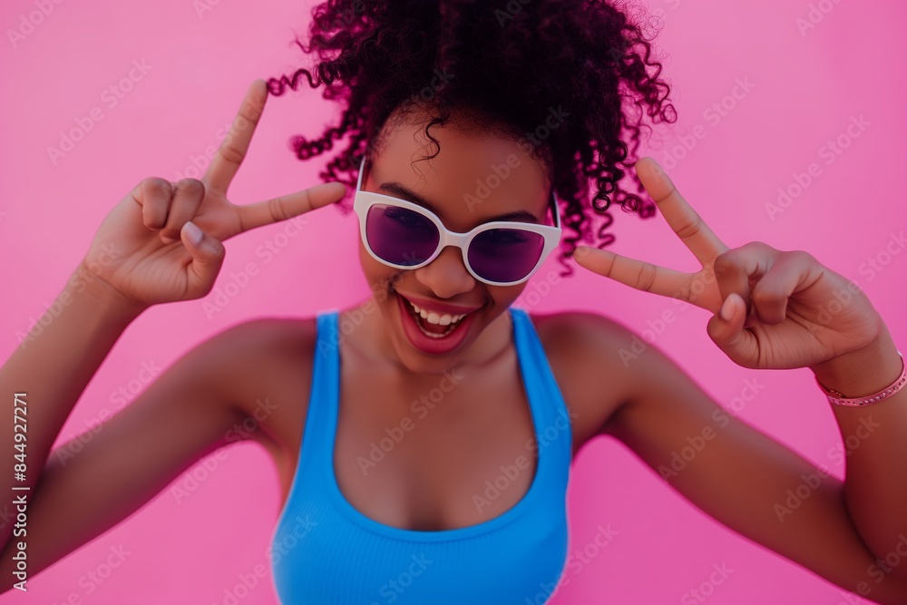 Sticker a young african american woman wearing sunglasses and making peace sign on a pink background