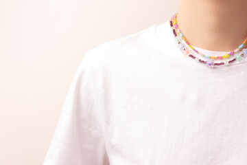 Multicolored handmade flower beads on a woman in a white t-shirt in front of beige background.