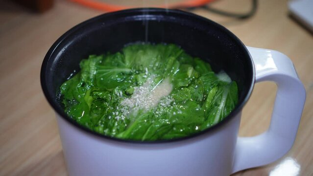 Sprinkling flavorings into the soup of green vegetables that is being cooked
