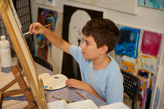 Young boy painting on canvas in art class workshop with vibrant background - Powered by Adobe