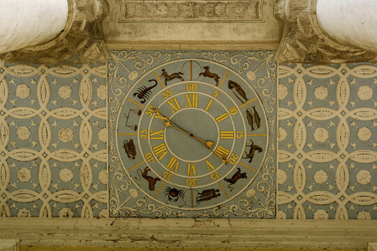 Gold ornate zodiac clock with Roman numerals and astrological symbols on background with detailed patterns and motifs. Ancient sciences and signs of the zodiac in architectural decorative elements