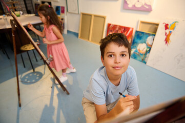 Children enjoying art class, drawing and painting with teacher in creative workshop