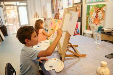 Kids painting and drawing in art class with teacher in workshop environment