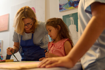 Teacher guiding young girl in art class painting and drawing workshop