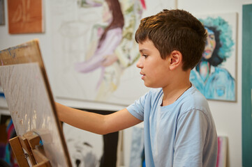 Young boy focused on painting during art class in the workshop