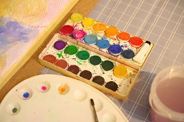 Colorful watercolor paint palette and paintbrush on a table in a vibrant art workshop, perfect for kids' creative projects.