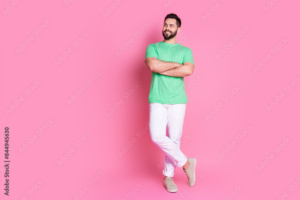 Poster Full size photo of cheerful guy dressed green t-shirt white pants holding palms crossed look empty space isolated on pink color background