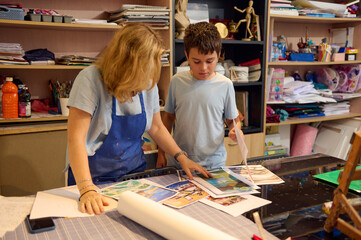 Kids have art class, drawing, painting with teacher in workshop. Teacher interacts with student, giving guidance on artistic projects.