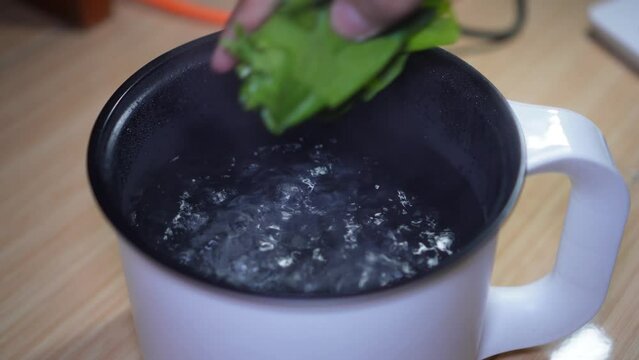 Putting green vegetables into a pot with hot water. Cooking green vegetables (collard green/mustard) on a white electric pot