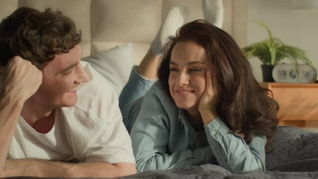 Man and woman lying on bed bedroom domestic cozy togetherness happy family couple laughing pampering boyfriend touching girlfriend nose feeling intimacy sweetheart loving sensuality beloved rent smile