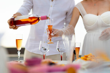 Bride and groom preparing for the bachelorette party pour white wine into glasses