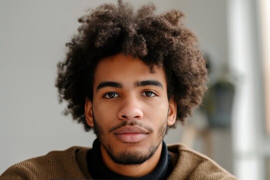 Portrait of a young entrepreneur with an afro hairstyle wearing a turtleneck sweater, looking seriously at camera in his home office