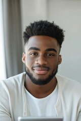 Obraz premium Young black man smiles while working from home on his digital tablet, showcasing a modern, casual office setup