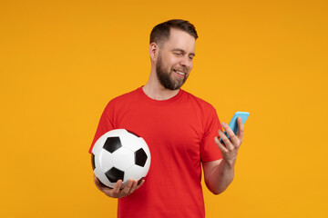 Studio shot of young smiling bearded man using his smartphone, making bets online at bookmaker's...