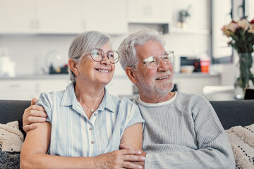 Dreamy middle aged senior loving retired family couple looking in distance, planning common future or recollecting memories, enjoying peaceful moment relaxing together on cozy sofa in living room. - Powered by Adobe