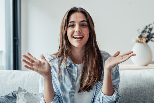 Head shot portrait smiling woman making video call to friends or relatives, using webcam, sitting on couch at home, happy young female blogger recording vlog, looking at camera, chatting online.