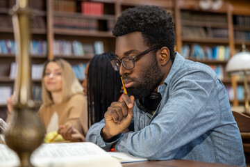 Curly-haired bearded african american man in the library looking thoughtful