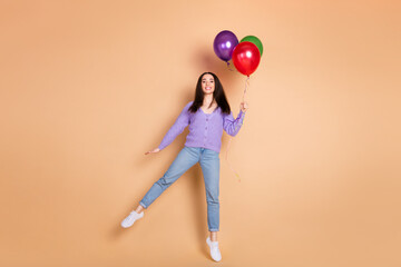 Full body portrait of nice young woman jump balloons wear cardigan isolated on beige color...
