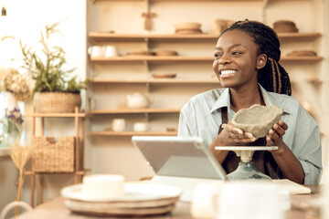 Fototapeta premium Contented african american woman showing a clay jar to the audience on online workshop
