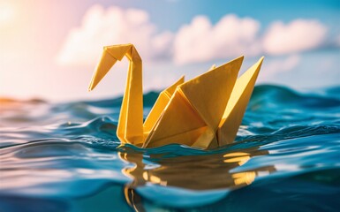 Fototapeta premium Close up of an yellow origami paper swan floating in the blue ocean water, with a background of a cloudy sunny sky.