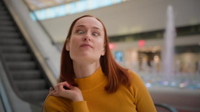 Portrait laughing funny smiling Caucasian ginger woman female girl buyer consumer grimacing customer fooling around making faces showing tongue hold paper bags looking camera shopping mall escalator