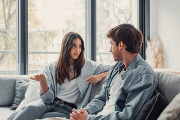 Young happy couple having fun talking laughing relaxing at home on couch, boyfriend embracing...