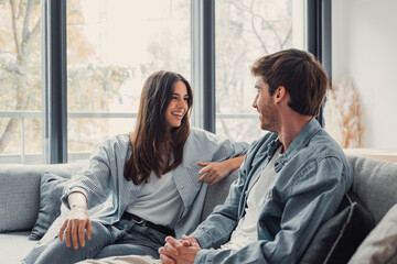 Young happy couple having fun talking laughing relaxing at home on couch, boyfriend embracing girlfriend telling funny joke sitting on sofa, humor in relationships, enjoying weekend together.