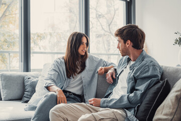 Young happy couple having fun talking laughing relaxing at home on couch, boyfriend embracing...