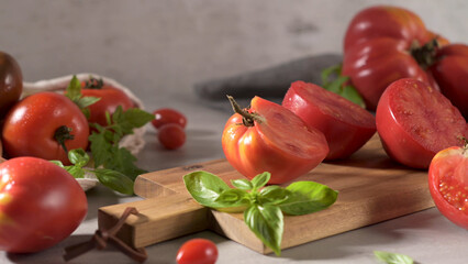 A variety of red tomatoes, whole and halved, on a wooden board, garnished with basil