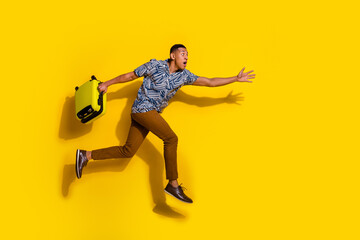 Full length photo of funky cool guy dressed print shirt holding baggage jumping running empty space isolated yellow color background