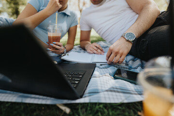 Focused students collaborating on homework with a laptop and notebook in a tranquil park setting...