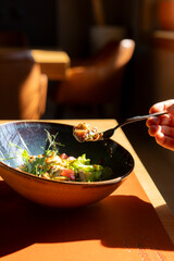 person enjoys a meal of fresh seafood salad with greens and vegetables, taking a bite with a fork