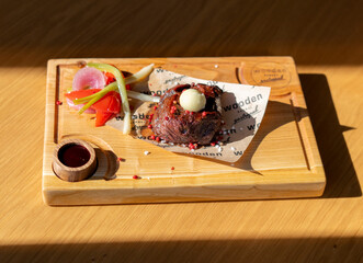 close-up shot of a grilled steak topped with butter and served on a wooden board with vegetables and a small dish of sauce