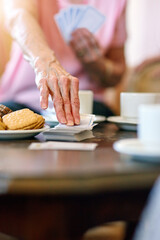 Elderly woman, table and hand with cards in retirement home for activity, hobby and fun on weekend. Games, senior person and relax with snack in living room for problem solving, strategy and contest