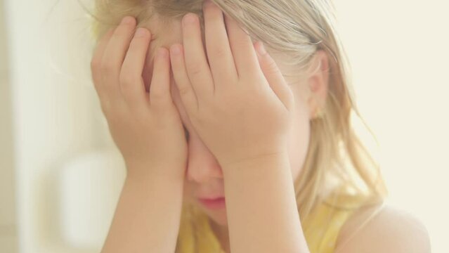 sweet child 5 years old, shy blonde girl covers eyes with hands, waiting surprise, capturing Playful innocence, emotional expression, tender moment, childhood charm, soft focus video