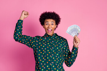 Portrait of ecstatic guy with wavy hairstyle dressed print shirt holding money win gambling raising...