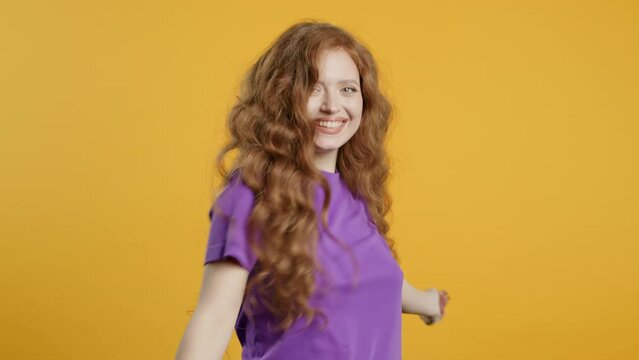 Happy ginger long haired woman dancing on yellow studio. Favorite music, smiling