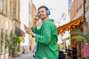 Rear view of happy relaxed man tourist in wireless headphones choosing, listening favorite...