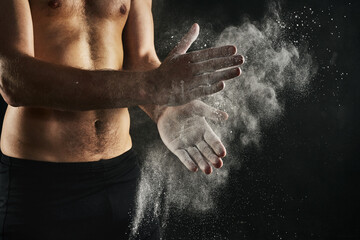 Fitness, hands and chalk in studio for exercise, weightlifting and start or gymnastics. Male gymnast, powder and preparation for workout, topless or muscular on black background with arm bands