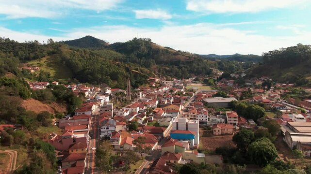 Aerial view of Delfim Moreira, Minas Gerais, Brazil, depicting a charming town nestled in a valley with rolling hills and dense forests.