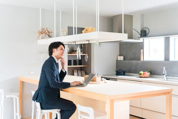 出勤前にダイニングテーブルでノートパソコンで仕事をするスーツ姿の若い男性ビジネスマン

