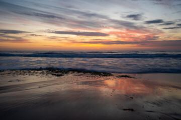 Fototapeta premium Sunrise over breaking waves beach orange yellow clouds