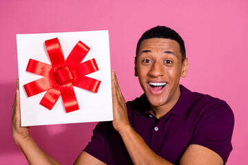 Photo portrait of attractive young man hold giftbox excited dressed stylish violet clothes isolated on pink color background