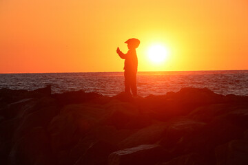 A figure silhouetted against the rising sun at a beach in Virginia while taking a selfie