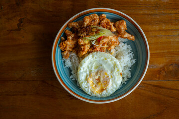 salted egg chicken rice bowl with egg served on blue bowl, over wooden table surface, in cafe environment