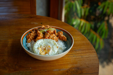 salted egg chicken rice bowl with egg served on blue bowl, over wooden table surface, in cafe environment